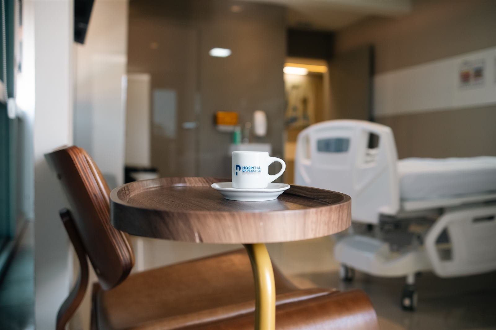 Xícara de café com a marca do hospital sobre mesa lateral, com o leito ao fundo